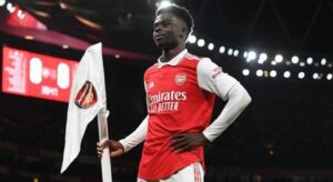 Jogador Bukayo Saka comemora gol segurando a abandeira do Arsenal.